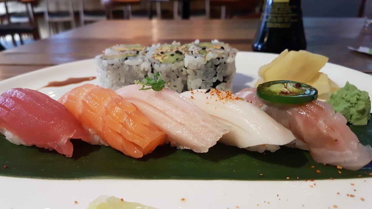 Nigiri lineup on a green leaf: tuna, salmon, and white fish with wasabi and pickled ginger