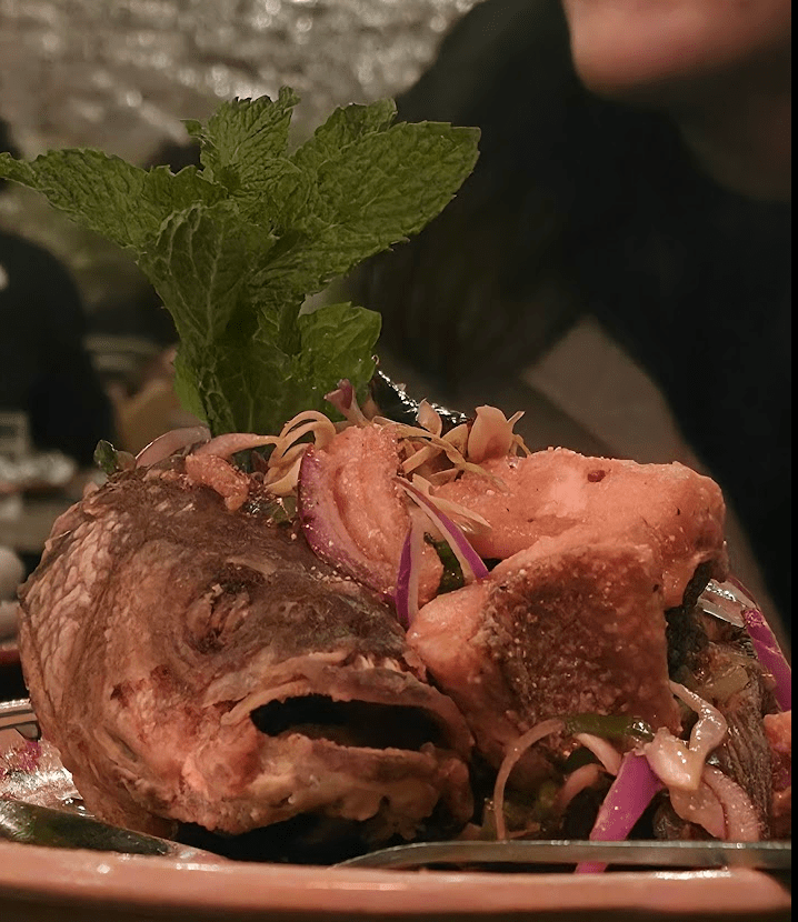 A beautifully presented dish featuring a whole fried fish topped with fresh mint and garnished with vibrant vegetables, served in a restaurant setting.